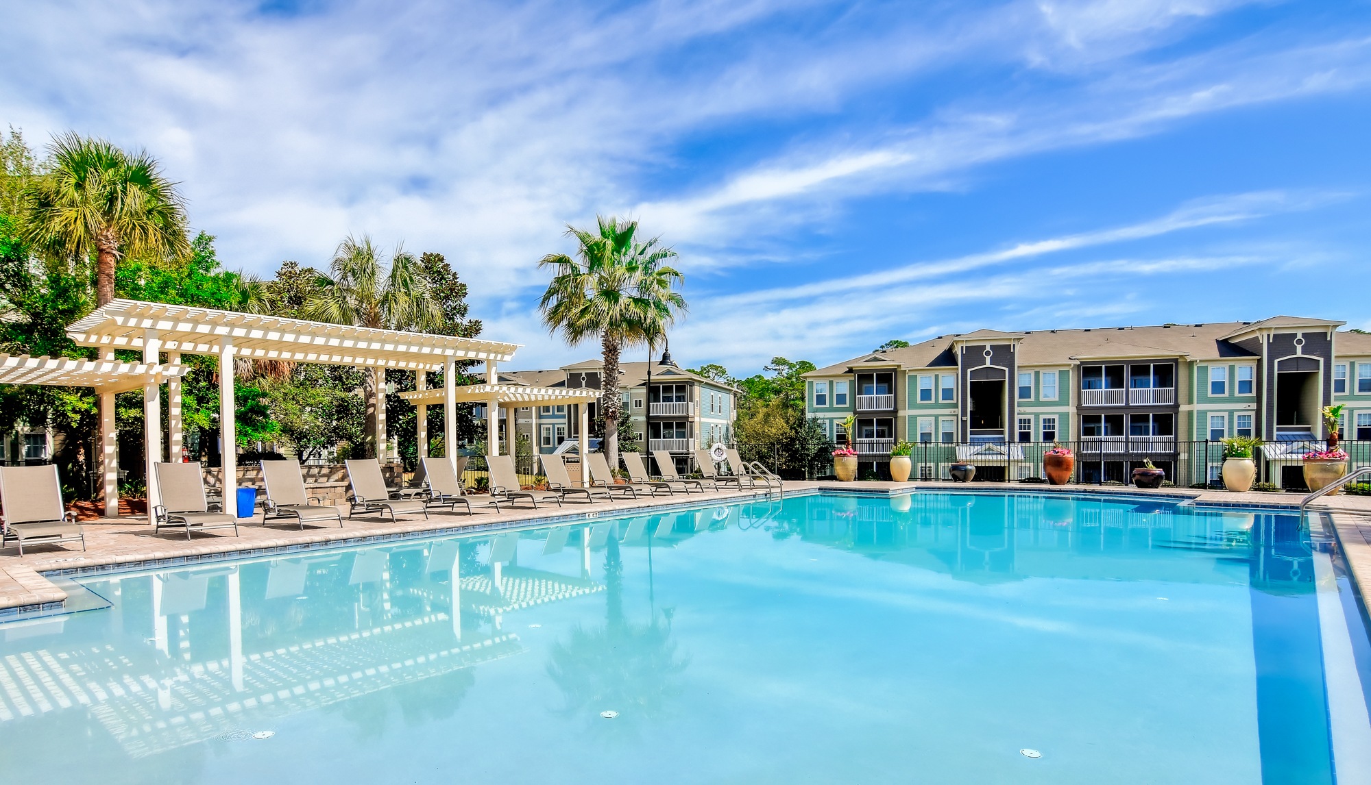 A large swimming pool with a white pergola and lounge chairs.